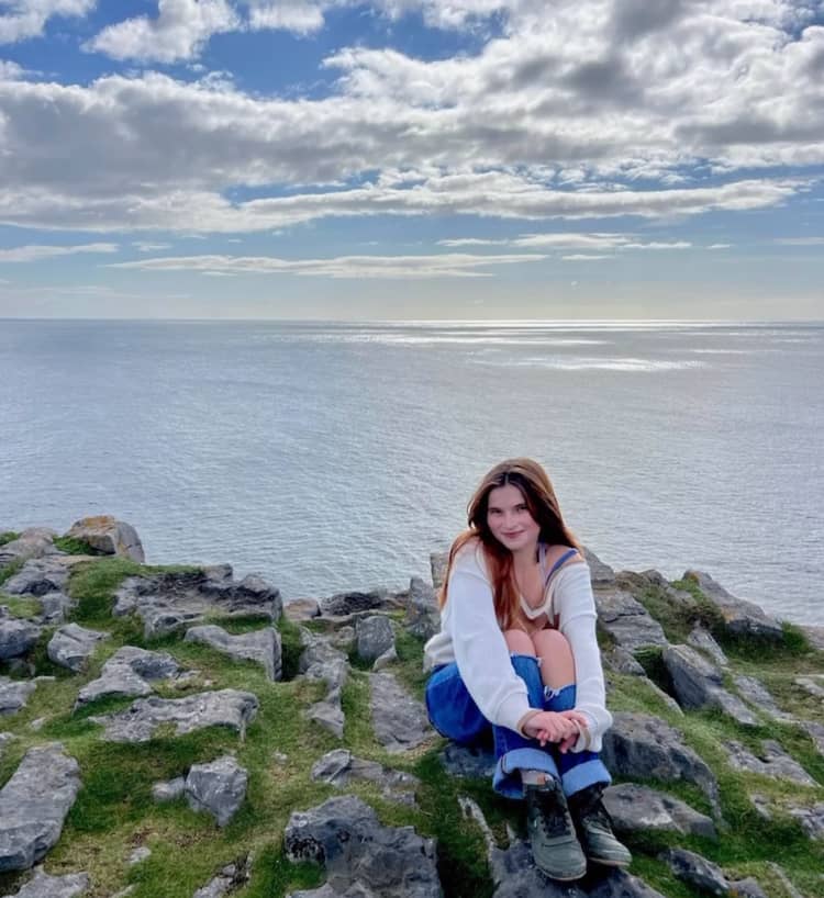 a person sitting on a rock ledge with water in the background