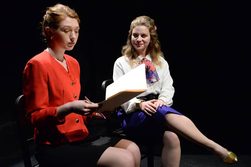 a person sitting on a chair holding a book and looking at another person