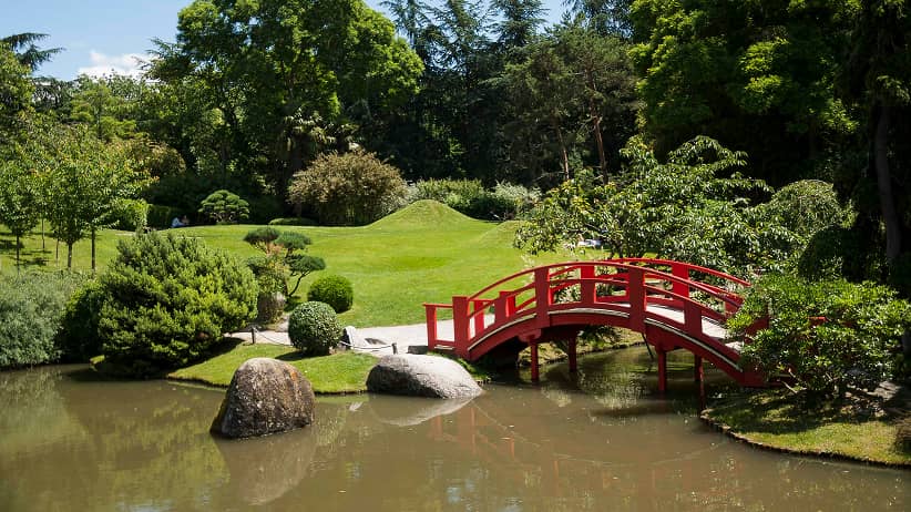 a red bridge over water with trees and grass