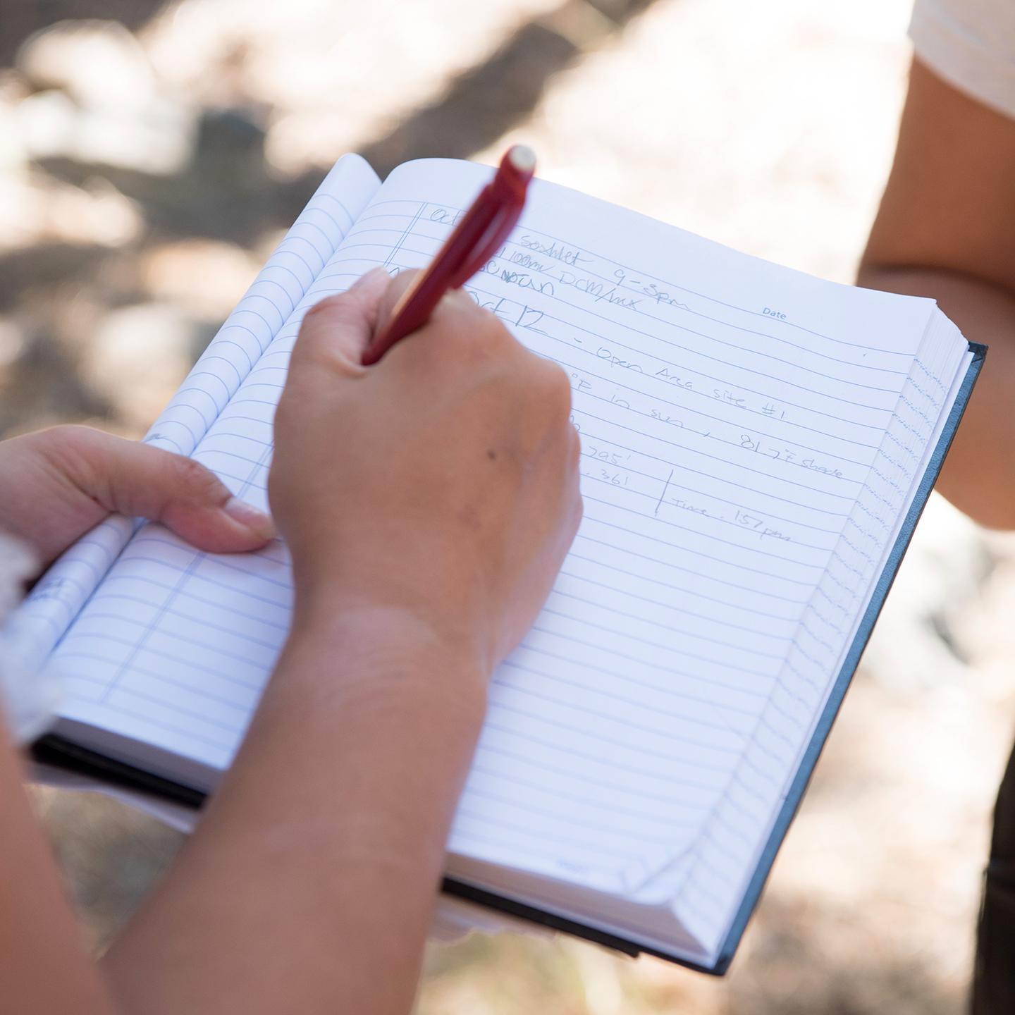 a person holding a pen and writing in a notebook