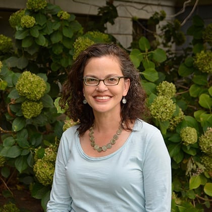 a woman smiling in front of a bush