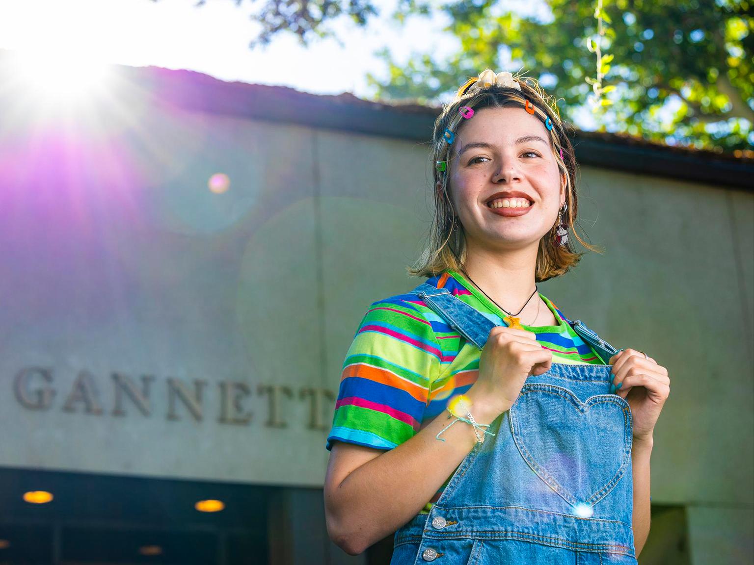 a woman smiling with rainbow colored shirt and denim overalls