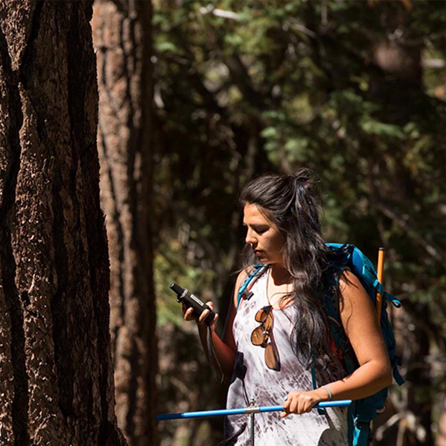 a woman with a backpack and a pole in a forest