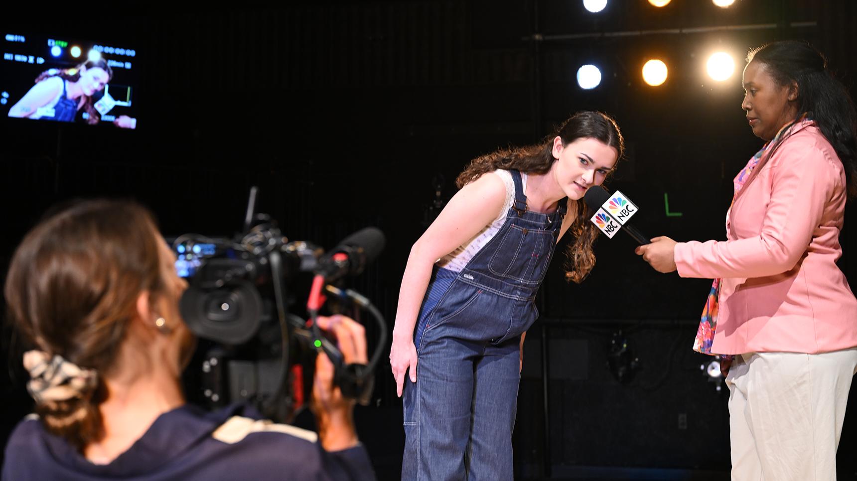 a woman in overalls with a microphone in front of a camera
