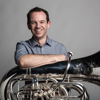 a man smiling with his arms crossed and a tuba