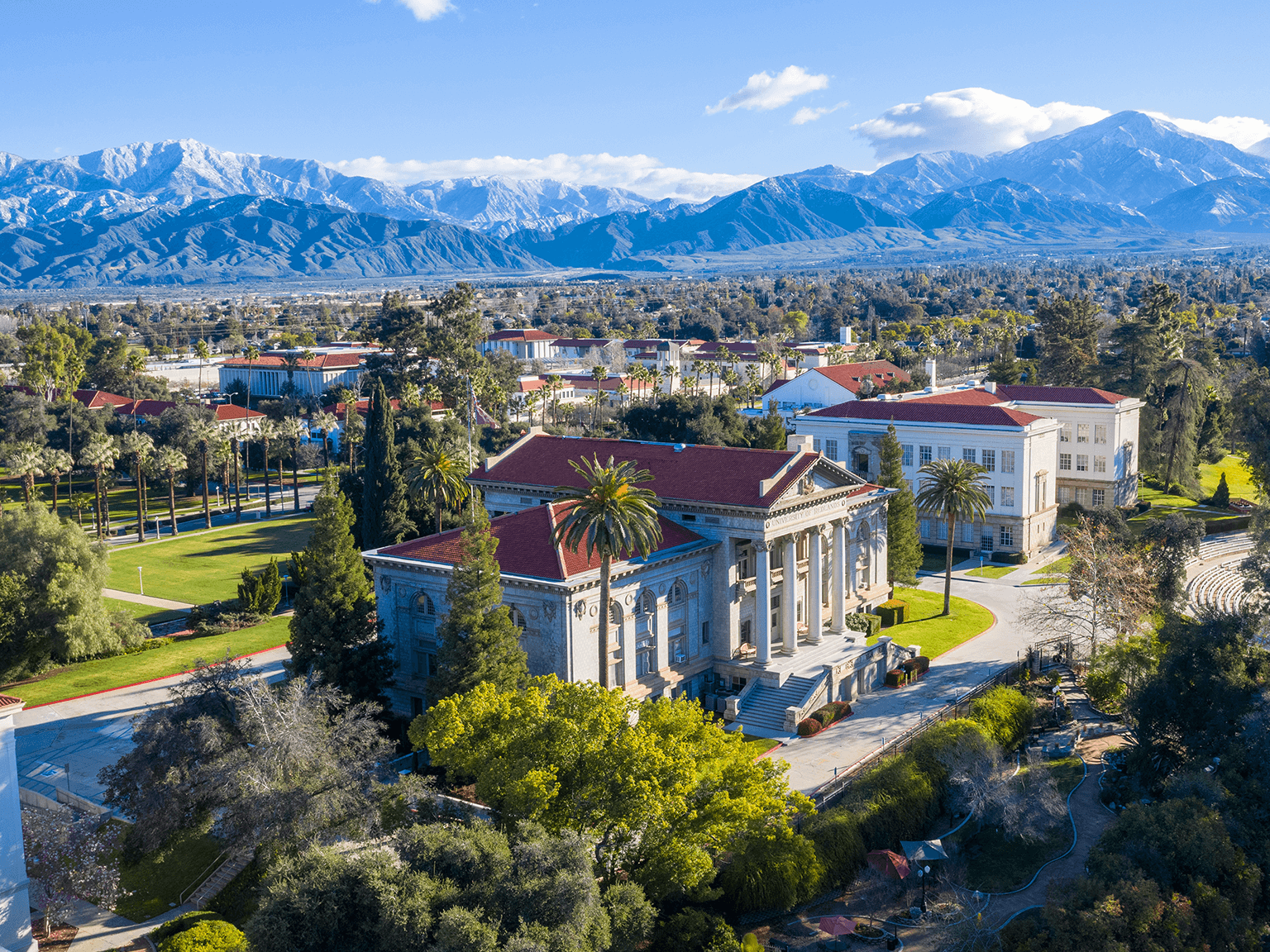 a large building with a red roof surrounded by trees and mountains