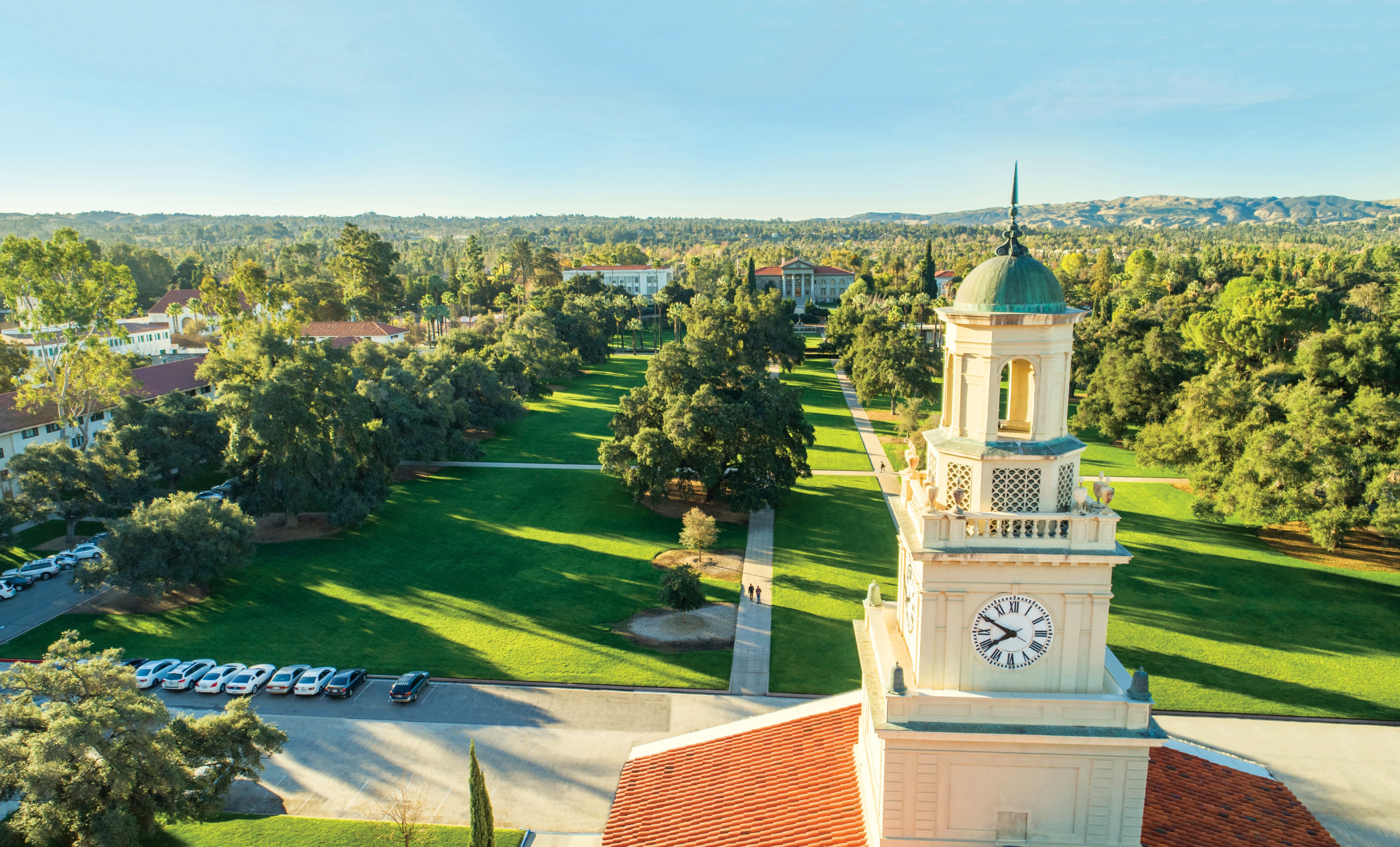 a tower with a clock on it and a lawn with trees and buildings