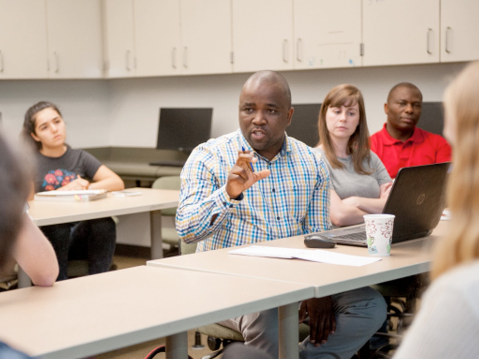 a man sitting at a table with a laptop and a group of people