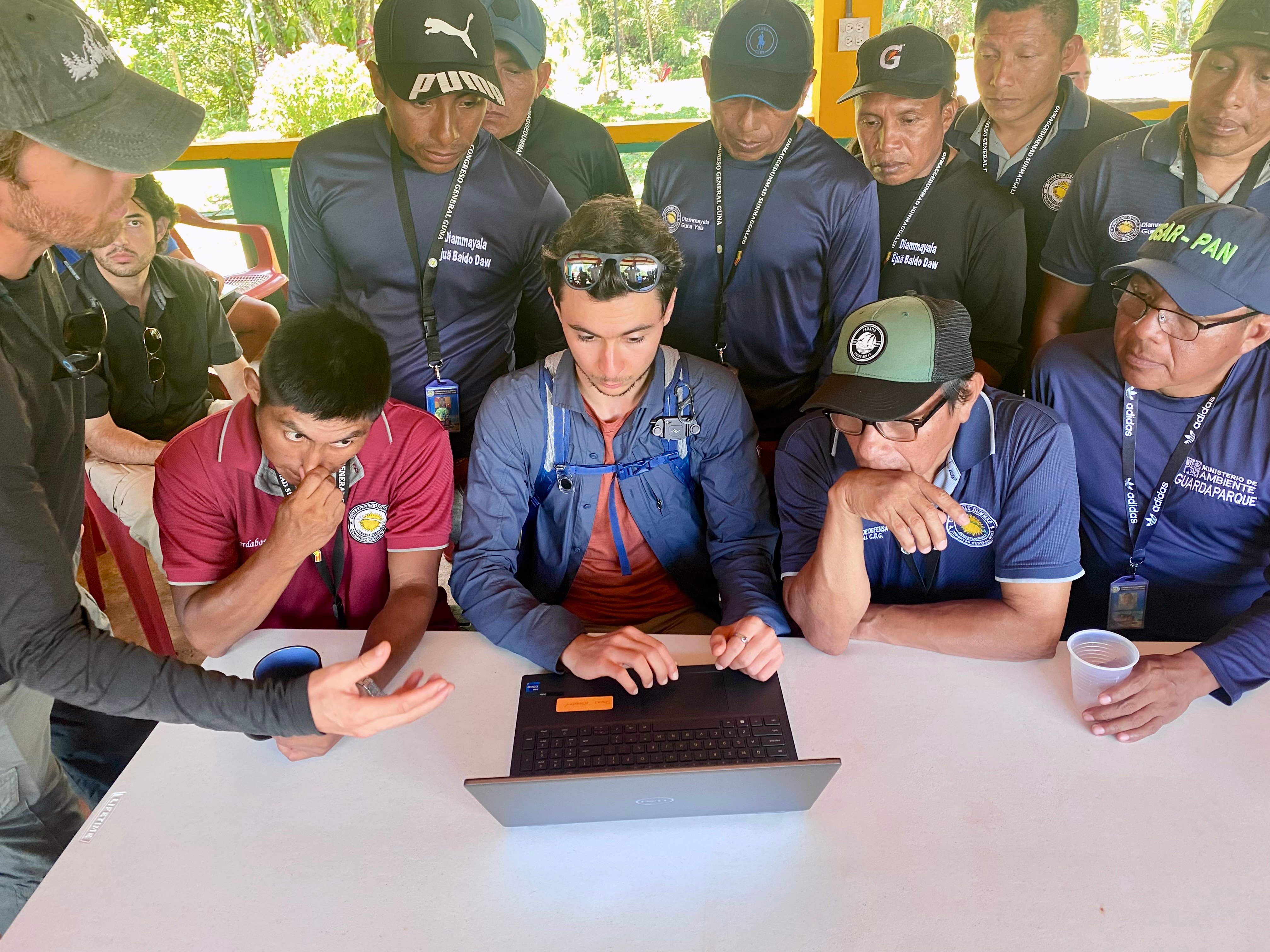 a group of people sitting around a table with a laptop