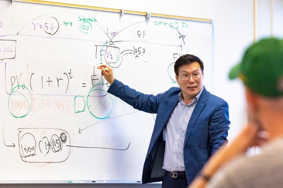 a man in a suit pointing at a whiteboard