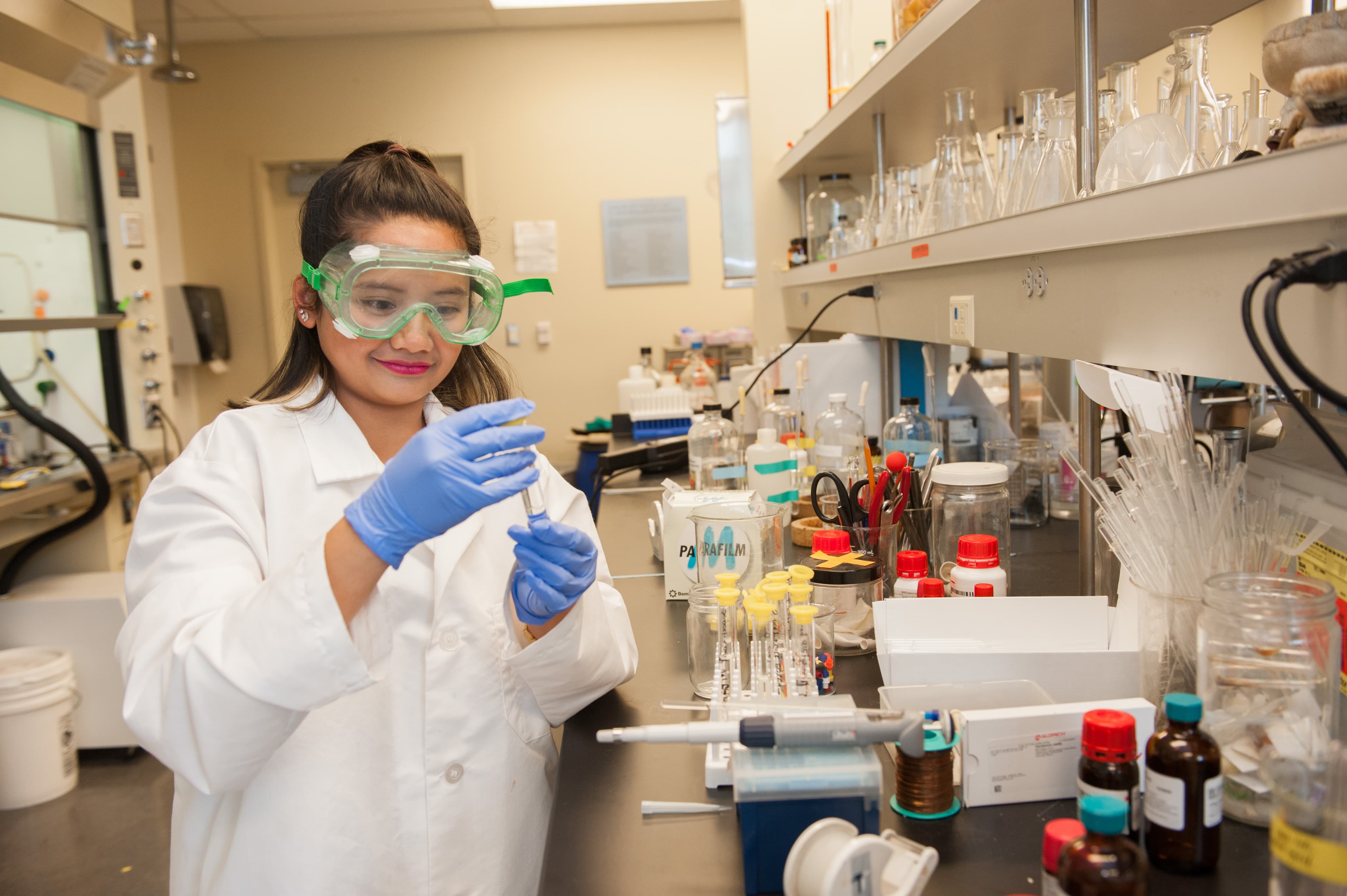 a woman wearing protective glasses and holding a test tube