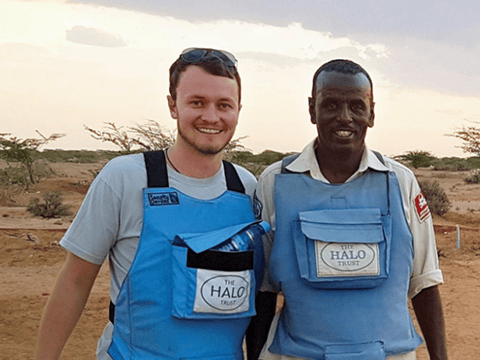 two men wearing blue vests standing in a desert