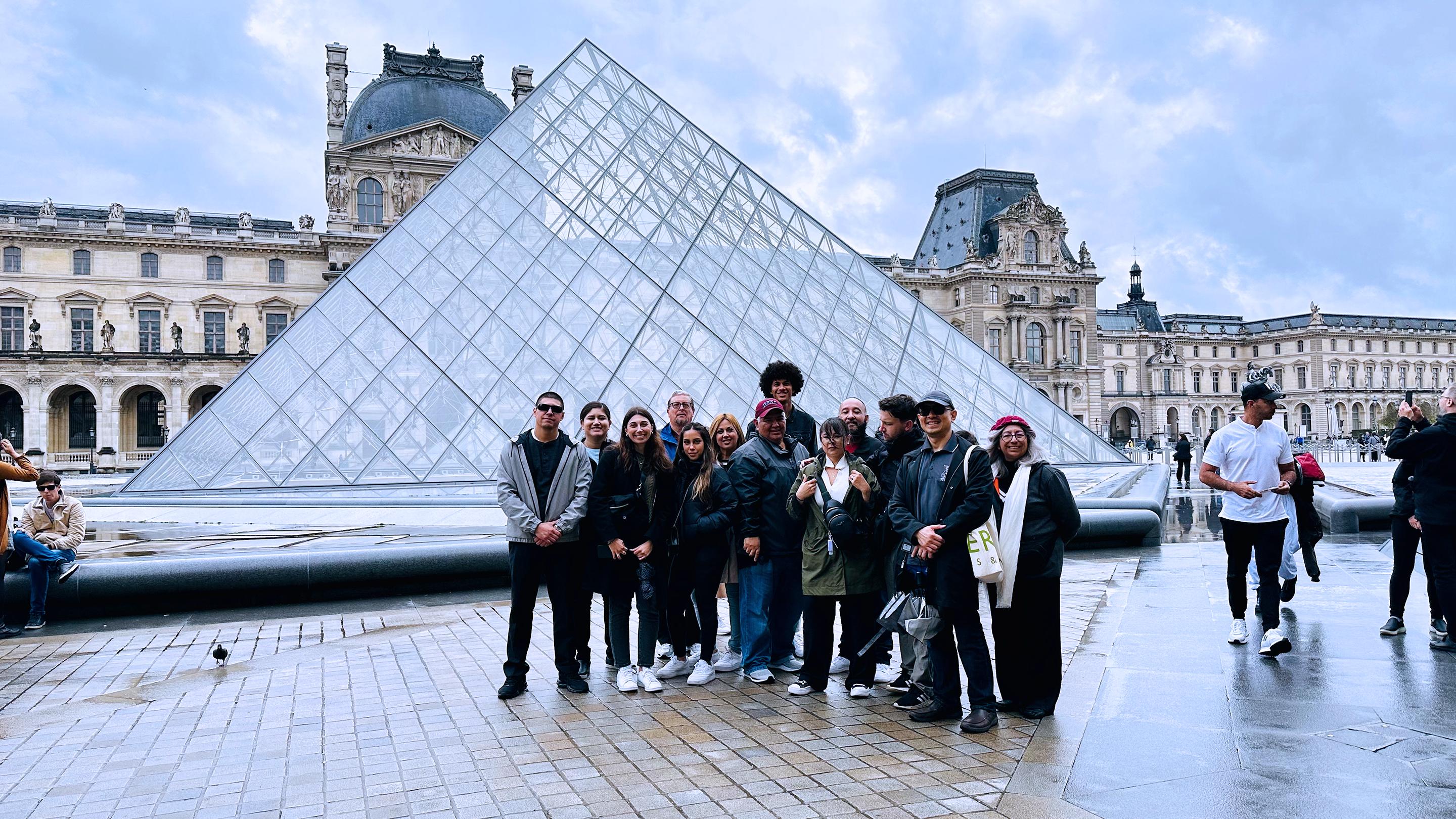 a group of people posing for a photo in front of a glass pyramid