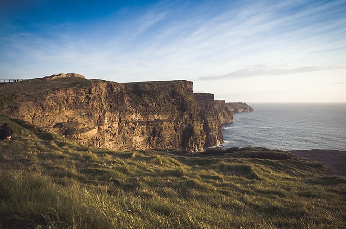 a cliff with grass and water in the background