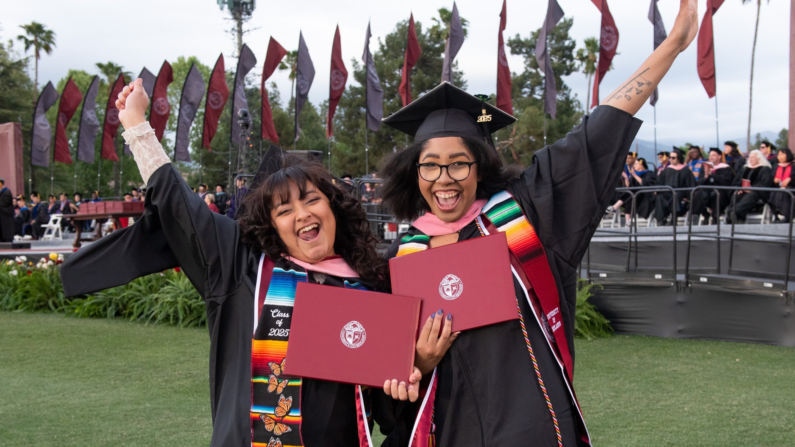 two women in graduation gowns and cap and gowns holding diplomas