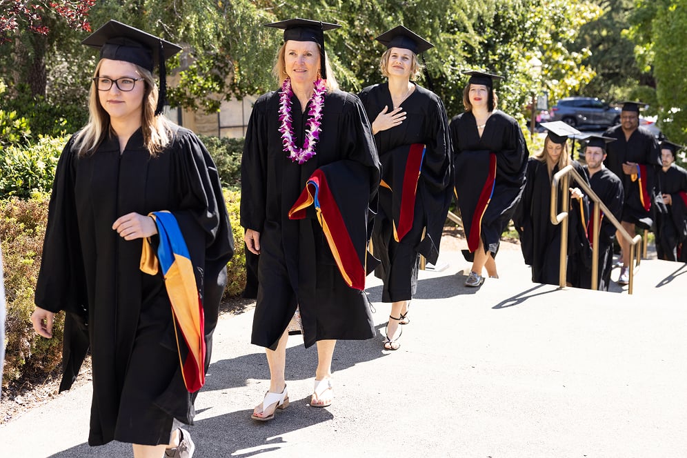 a group of women in graduation gowns and caps walking down a sidewalk