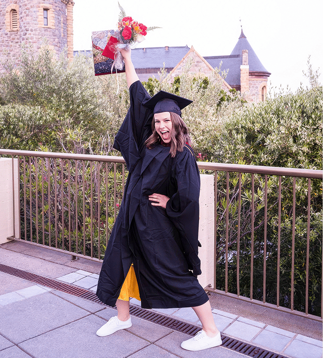 a woman in a graduation gown and cap holding a bouquet of flowers