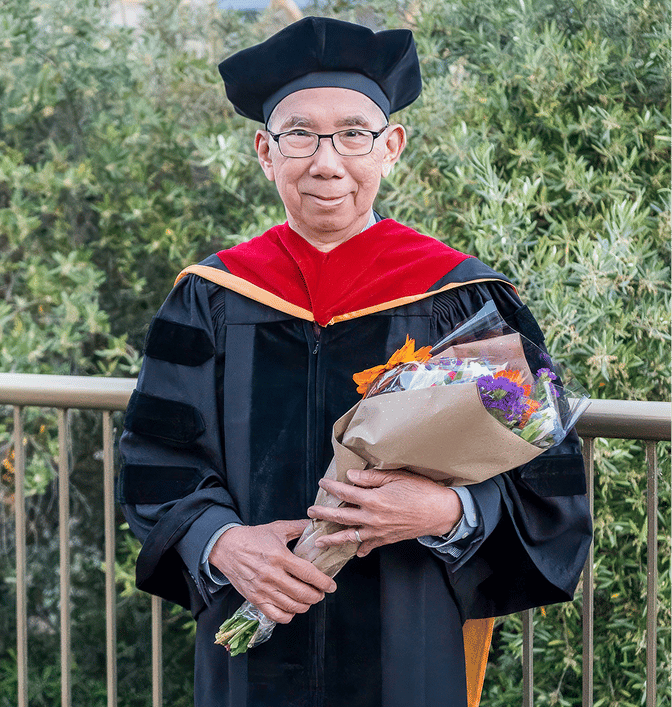 a man in a graduation gown holding flowers