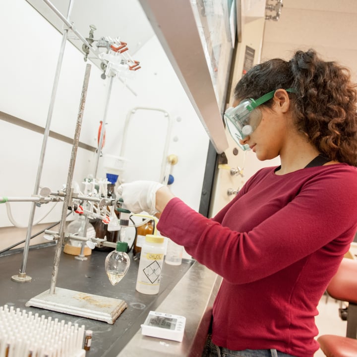 a woman wearing safety goggles and gloves working in a lab