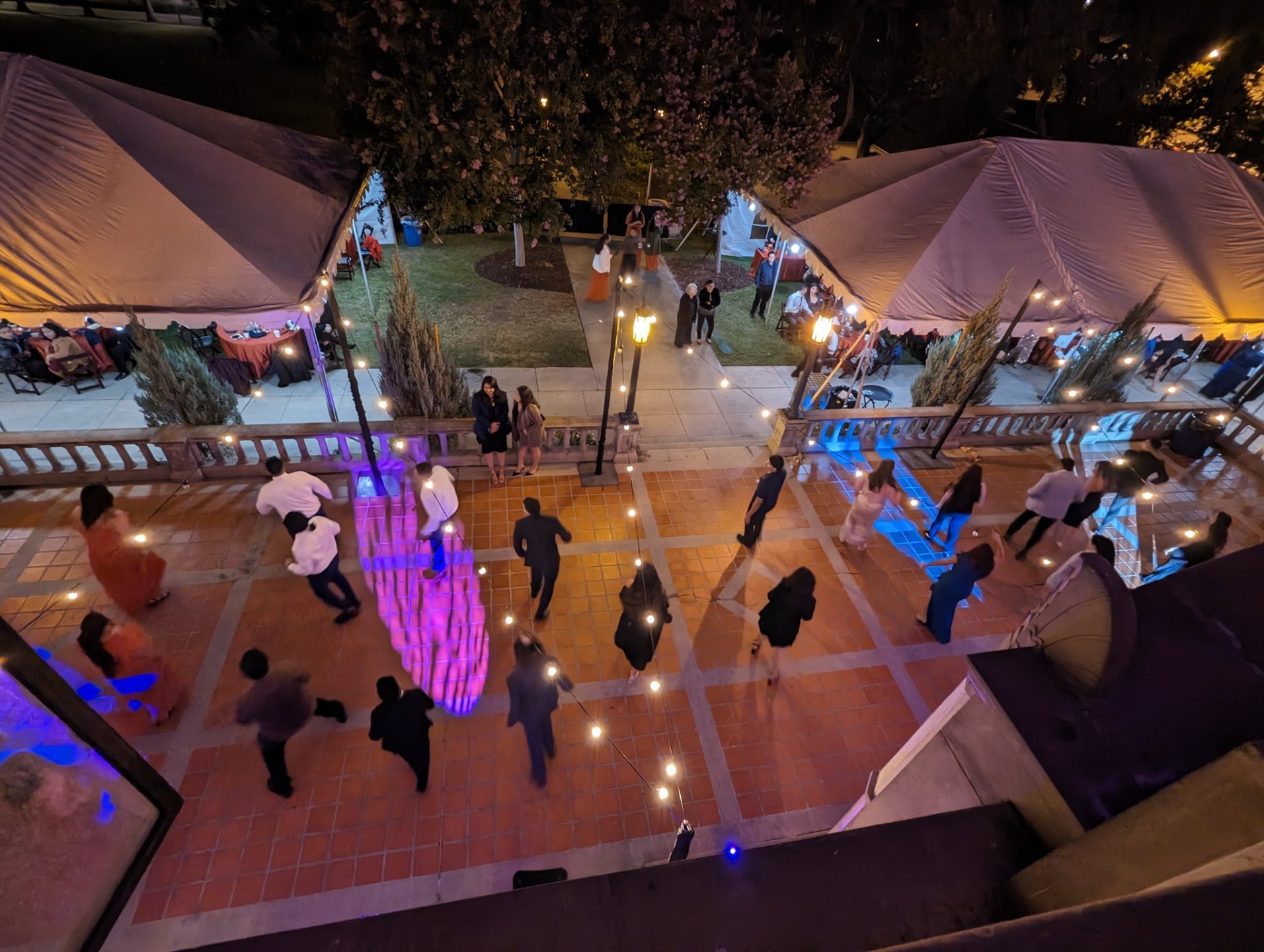 a group of people walking around a courtyard with tents and trees