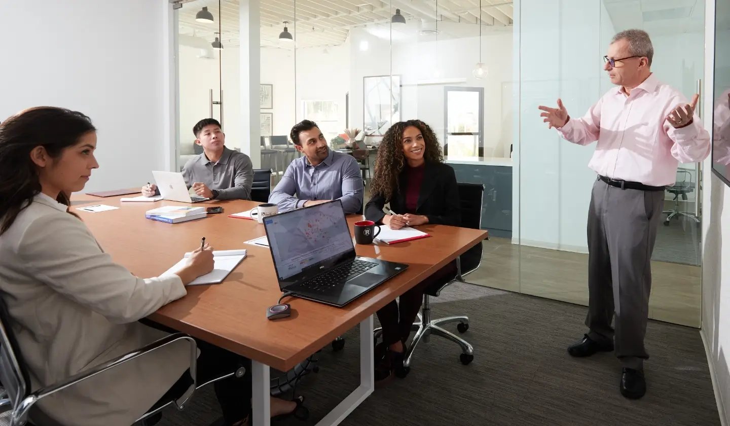 a man standing in front of a man pointing at a whiteboard