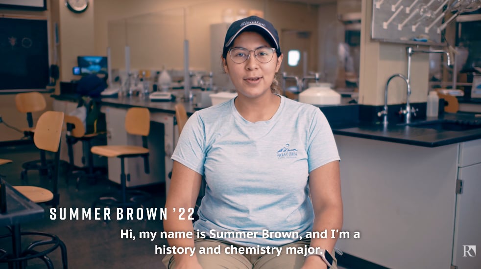 a woman in a blue cap and glasses sitting in a room with a science lab