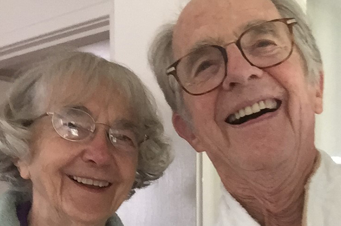 A couple, both wearing glasses, smile and take a selfie together.