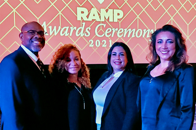 Four people stand together in front of a presentation screen at an award ceremony.
