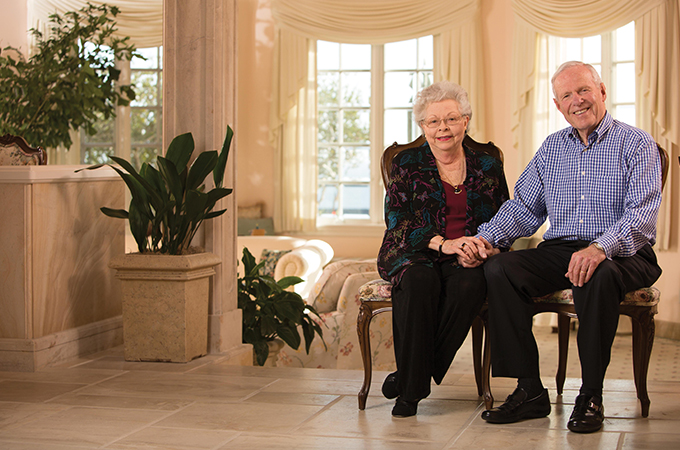 The Hunsakers sit in the foyer of a grand room, holding hands and smiling.