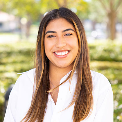 Zharit Brand Robles smiling outdoors in a white shirt with greenery in the background.