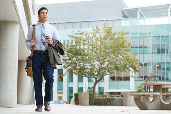 Man in business casual clothes walking outside a campus building