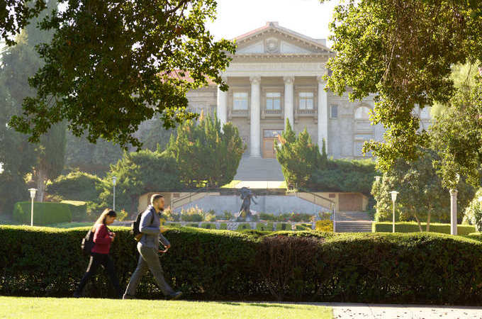Two people walk in front of the Administration Building and REDLANDS lawn