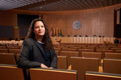Montserrat Pineda smiling while seated in an empty city council chamber.
