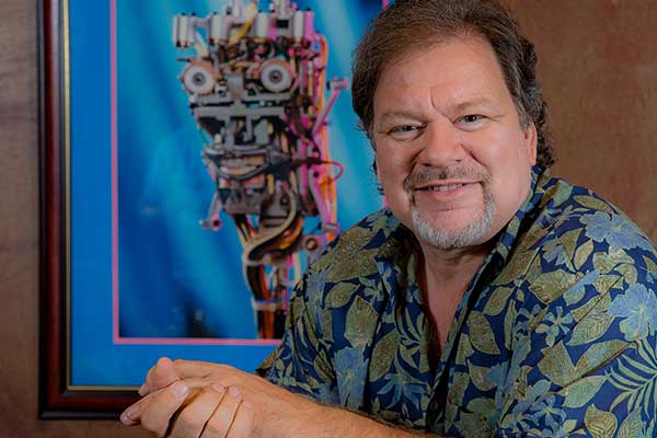 Garner Holt sitting front of a framed picture of a robot with exposed internal workings.