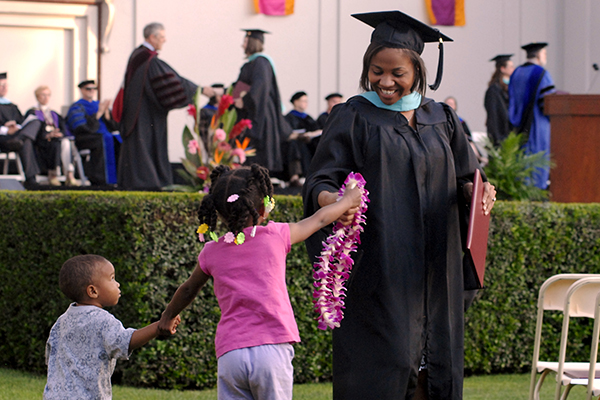 School of Education graduate being handed a lei by child during commencement.