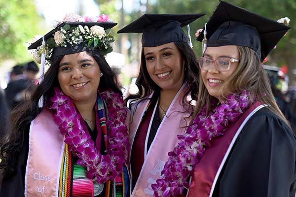 three female students smiling during commencement wearing caps, gowns, and floral leis