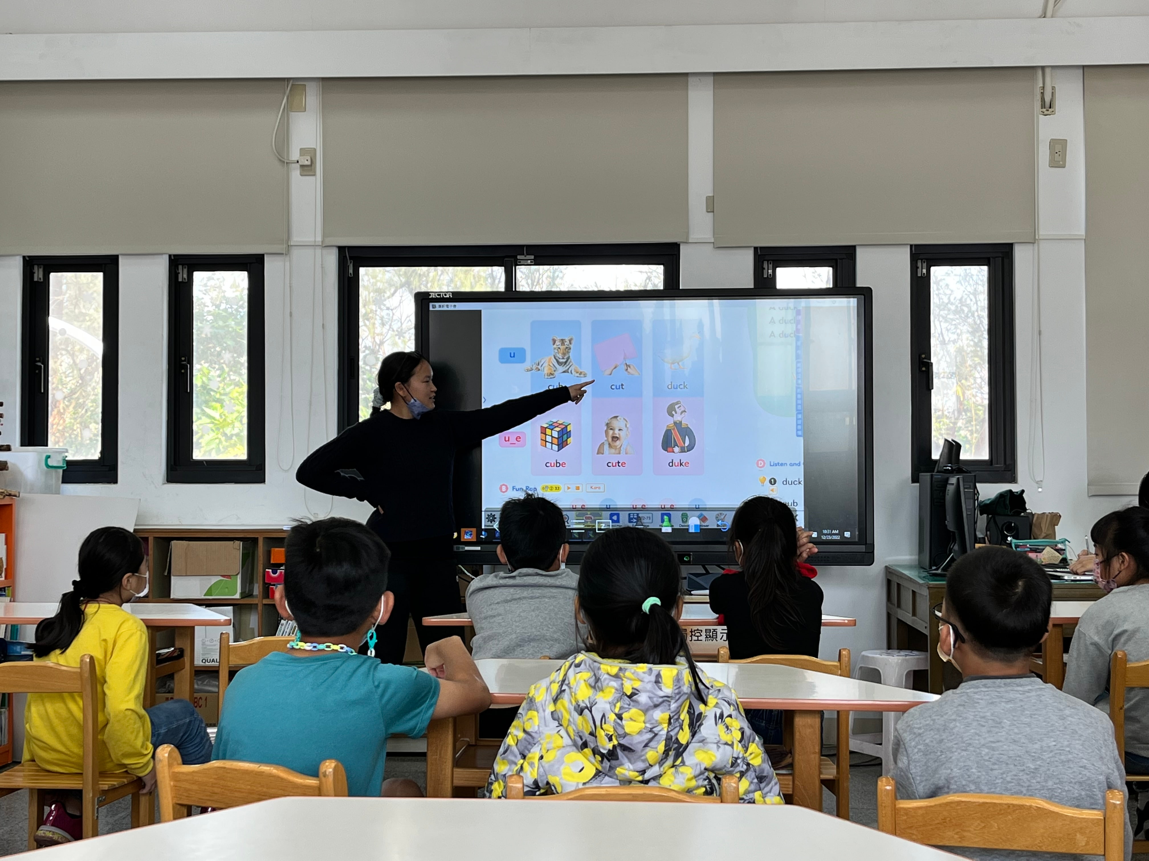 a person standing in front of a large screen with a group of kids sitting at desks