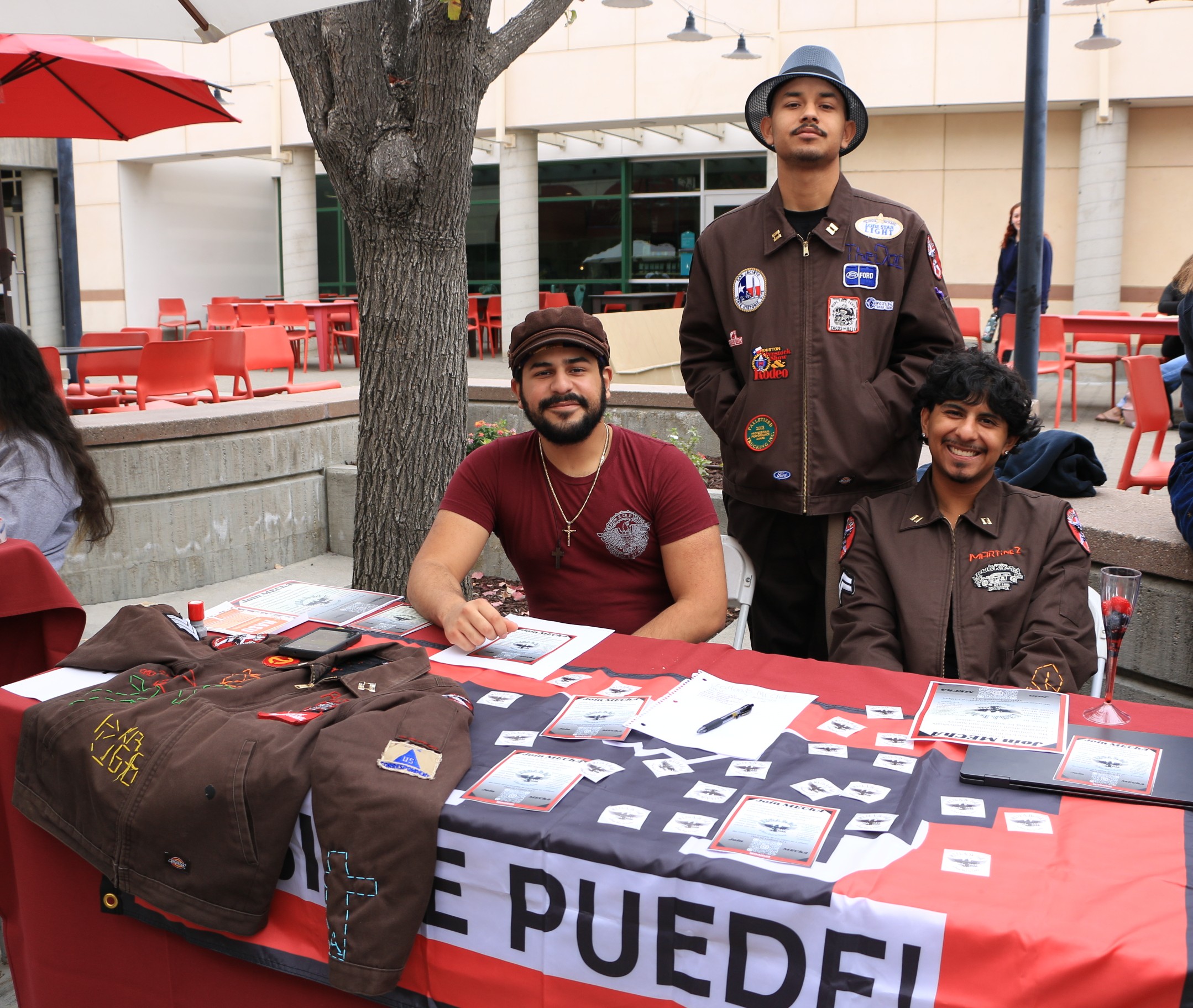 Three students pose behind a table displaying decorated jackets and printed materials at the Involvement Fair.